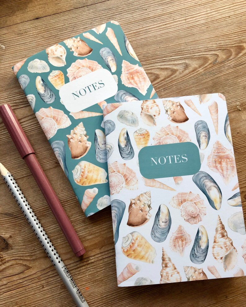May include: Two teal and white notebooks with a seashell and mussel pattern. The notebooks have the word "NOTES" printed on the front cover.