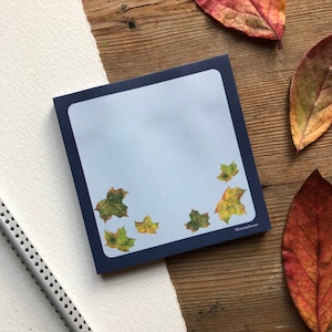 Könnte beinhalten: Ein blauer Notizblock mit hellblauem Hintergrund und weißem Rand. Der Notizblock hat ein Design aus fallenden Herbstblättern in Grün-, Gelb- und Brauntönen. Der Text "@jennymyheart" befindet sich in der rechten unteren Ecke.