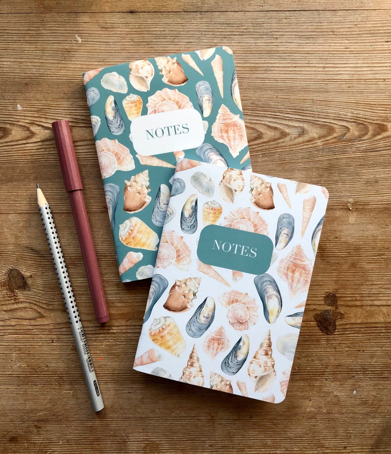 May include: Two small notebooks with a seashell and mussel design. The notebooks are teal and white with the word "NOTES" printed on the front.