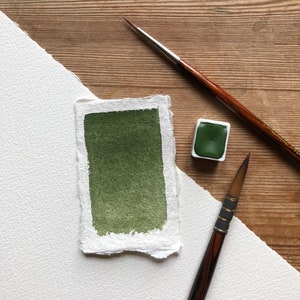 May include: A green watercolor paint pan with a brush and a sample of the paint on a white paper background.
