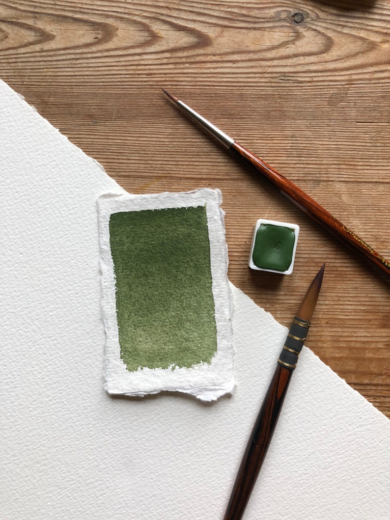 May include: A green watercolor paint pan with a brush and a sample of the paint on a white paper background.