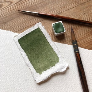 May include: A green watercolor paint pan with a brush and a sample of the paint on a piece of paper.
