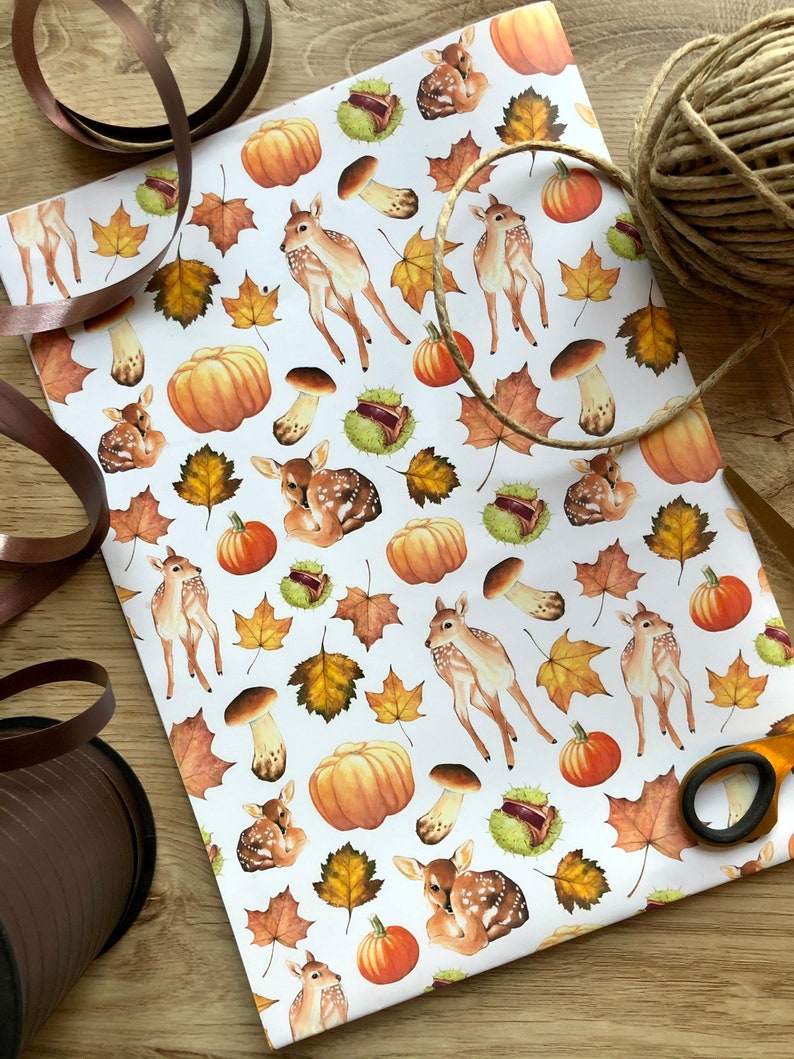 May include: White wrapping paper with a repeating pattern of brown and orange pumpkins, brown mushrooms, brown leaves, and brown deer.