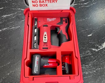Könnte beinhalten: Ein roter Milwaukee Werkzeugkoffer, geöffnet, um einen roten Tacker, Akku und Ladegerät zu zeigen. Der Deckel trägt den Text "INSERT ONLY, NO TOOLS, NO BATTERY, NO BOX". Der Koffer steht auf einer dunklen Oberfläche.