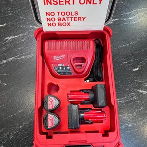 May include: Red Milwaukee M12 battery charger and batteries in a red case. The case lid has a white sign that reads "INSERT ONLY, NO TOOLS, NO BATTERY, NO BOX". The case contains a charger, two batteries, and two battery-powered tools.
