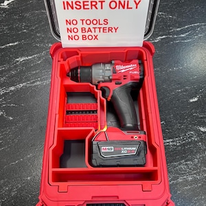 May include: A red and black Milwaukee drill and battery set in a red plastic case. The case has a clear lid with the text "INSERT ONLY, NO TOOLS, NO BATTERY, NO BOX". The drill is black and red, and the battery is black.