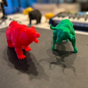 May include: A red bear figurine facing a green bull figurine. Both figurines are standing on a black surface.
