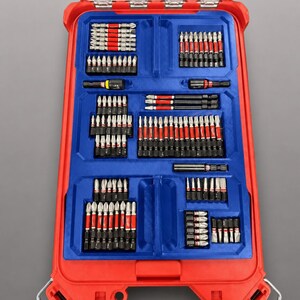 Puede incluir: Un maletín de herramientas de plástico rojo con un inserto interior azul que contiene varias puntas de taladro y destornillador de metal. El maletín tiene una tapa transparente y el texto: INSERT ONLY - NO TOOLS - NO BATTERY - NO BOX.