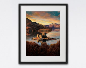 May include: A framed photograph of a castle on a small island in a loch. The castle is made of stone and has a pointed roof. The loch is surrounded by trees and mountains. The sky is a beautiful sunset colour.