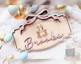 May include: A wooden sign with a pink bow and the text "A special Easter delivery for Brooke". The sign features a laser-cut design with a bunny rabbit illustration.