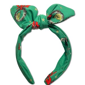 May include: Green headband with a bow and a Christmas-themed print featuring a wreath, stars, and a red and white figure.