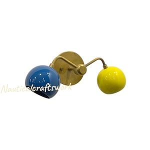 May include: A wall-mounted light fitting with a brass finish. It features two spherical lamps, one in a glossy blue and the other in yellow. The fitting has a circular base and curved arms extending to the lamps.