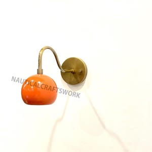 Puede incluir: Una lámpara de pared de latón con un brazo curvo y una pantalla de vidrio naranja.