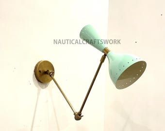 May include: A brass wall-mounted light fixture with a mint green shade and a brass arm. The shade has a perforated pattern and the arm is adjustable.