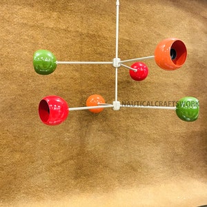 Könnte beinhalten: Eine moderne Leuchte im Mid-Century-Stil mit fünf runden, farbigen Schirmen. Die Schirme sind rot, grün, orange und ein dunkleres Orange. Die Leuchte ist mit einer weißen Metallstange an der Decke befestigt.