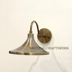 Peut inclure: Une applique murale en laiton avec un bras incurvé et un abat-jour en forme de cloche. L'applique a un design simple et élégant et serait un excellent ajout à n'importe quelle maison.