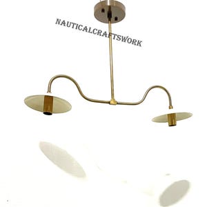 Könnte beinhalten: Eine zweilampige Hängeleuchte aus Messing mit weißen Metallabdeckungen. Die Leuchte hat ein gebogenes Armdesign und einen schlichten, modernen Stil.