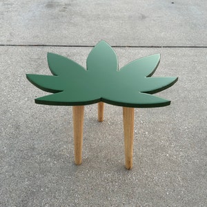 May include: A green leaf-shaped side table with four wooden legs. The table is made of wood and has a dark green finish.