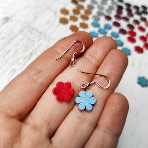 Könnte beinhalten: Ein Paar Ohrringe mit silbernen Haken und kleinen Blumenanhängern. Ein Anhänger ist rot und der andere ist hellblau.