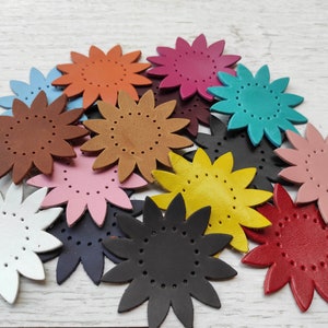 Könnte beinhalten: Sortiment aus bunten Lederblumenformen mit einem Loch in der Mitte. Die Blumen sind in verschiedenen Farben, darunter Rot, Rosa, Blau, Gelb, Braun und Schwarz.