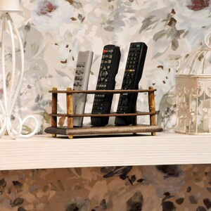 May include: A wooden remote control holder with three remotes, two black and one white, on a white shelf with a white birdcage and a white metal decorative stand.