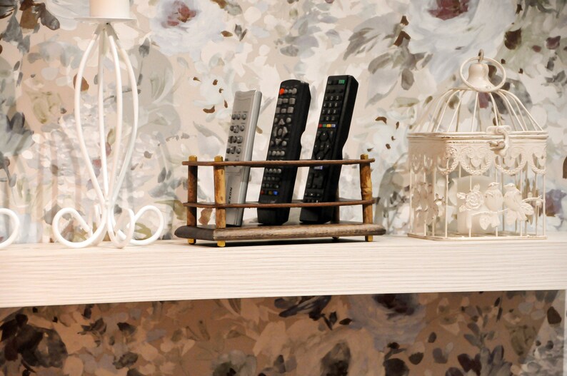 May include: A wooden remote control holder with three remotes, two black and one white, on a white shelf with a white birdcage and a white metal decorative stand.