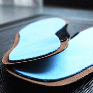 May include: Two blue insoles with brown leather backing. The insoles are designed to fit inside shoes.