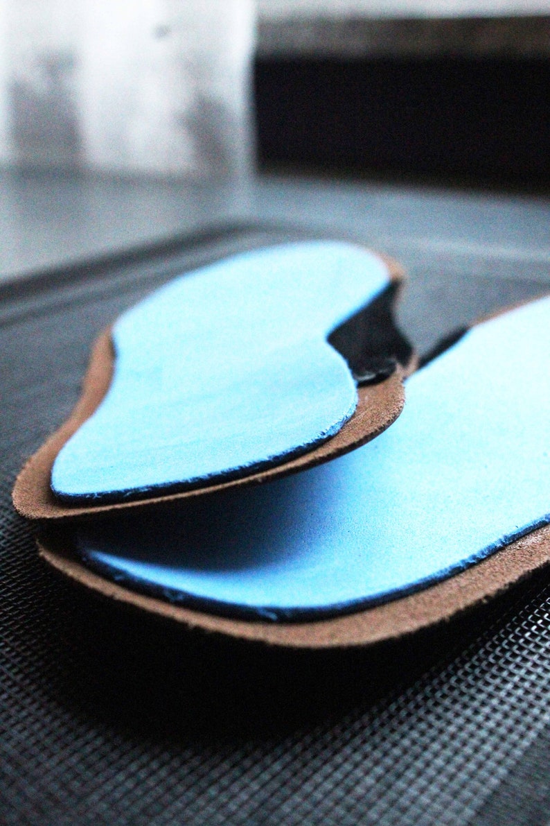 May include: Two blue insoles with brown leather backing. The insoles are designed to fit inside shoes.