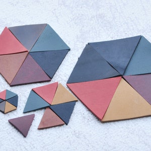 Może przedstawiać: Zestaw sześciu sześciokątnych płytek geometrycznych w różnych odcieniach czerwieni, brązu, fioletu, błękitu i turkusu. Płytki są wykonane z fakturowanego materiału i ułożone w wzór.