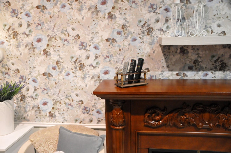 May include: A wooden fireplace mantel with a carved design and a shelf on top. The shelf has a metal remote control holder with four remotes inside. The wall behind the mantel has a floral wallpaper with a light blue and brown color scheme.