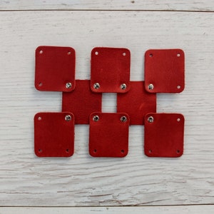 May include: A set of eight red leather squares with silver metal eyelets. The squares are arranged in a grid pattern.