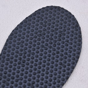May include: Close-up of a black rubber shoe sole with a textured pattern of small stars.