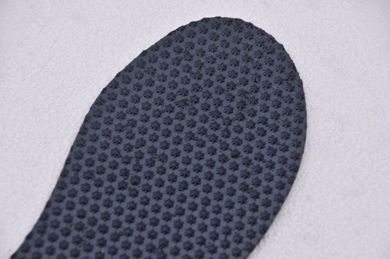 May include: Close-up of a black rubber shoe sole with a textured pattern of small stars.