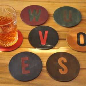 Könnte beinhalten: Sechs runde Lederuntersetzer in verschiedenen Farben und Buchstaben. Die Buchstaben ergeben das Wort "WOVES".