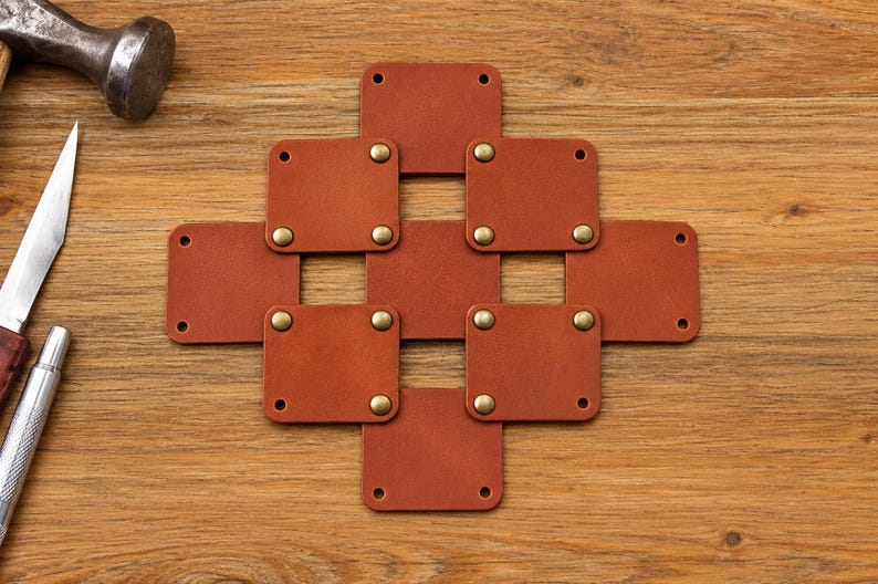 May include: A geometric arrangement of eight square, tan leather patches connected by brass-colored metal rivets. The leather squares are linked to form a cross-like pattern with open spaces between them, featuring pre-punched holes at the corners.