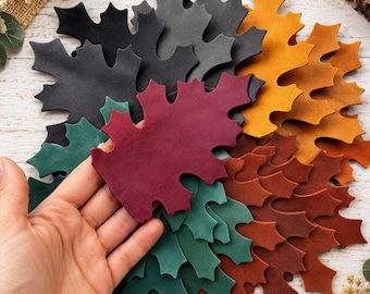 May include: A collection of die-cut leaf shapes made from smooth material in various colors including black, deep red, forest green, mustard yellow, and burnt orange. The leaves feature pointed lobes and are layered together in a cluster.