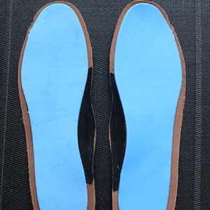 May include: A pair of blue shoe insoles with black arch support and brown edges.