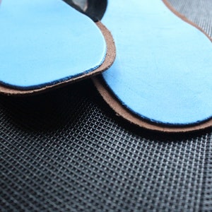 May include: Two brown leather insoles with blue foam padding. The insoles are on a black textured surface.