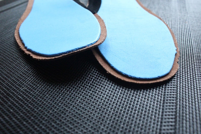 May include: Two brown leather insoles with blue foam padding. The insoles are on a black textured surface.