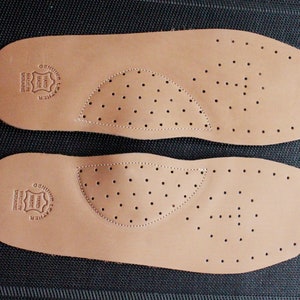 May include: Two brown leather insoles with a perforated design. The insoles have a circular logo that reads "Genuine Leather Hand Made Denmark".