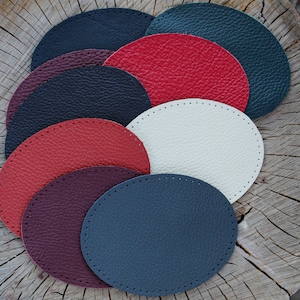 Op de afbeelding: Een set van acht leren cirkels in verschillende kleuren, waaronder rood, wit, zwart en blauw. De cirkels zijn gestapeld, met de grootste cirkel onderaan en de kleinste cirkel bovenaan.