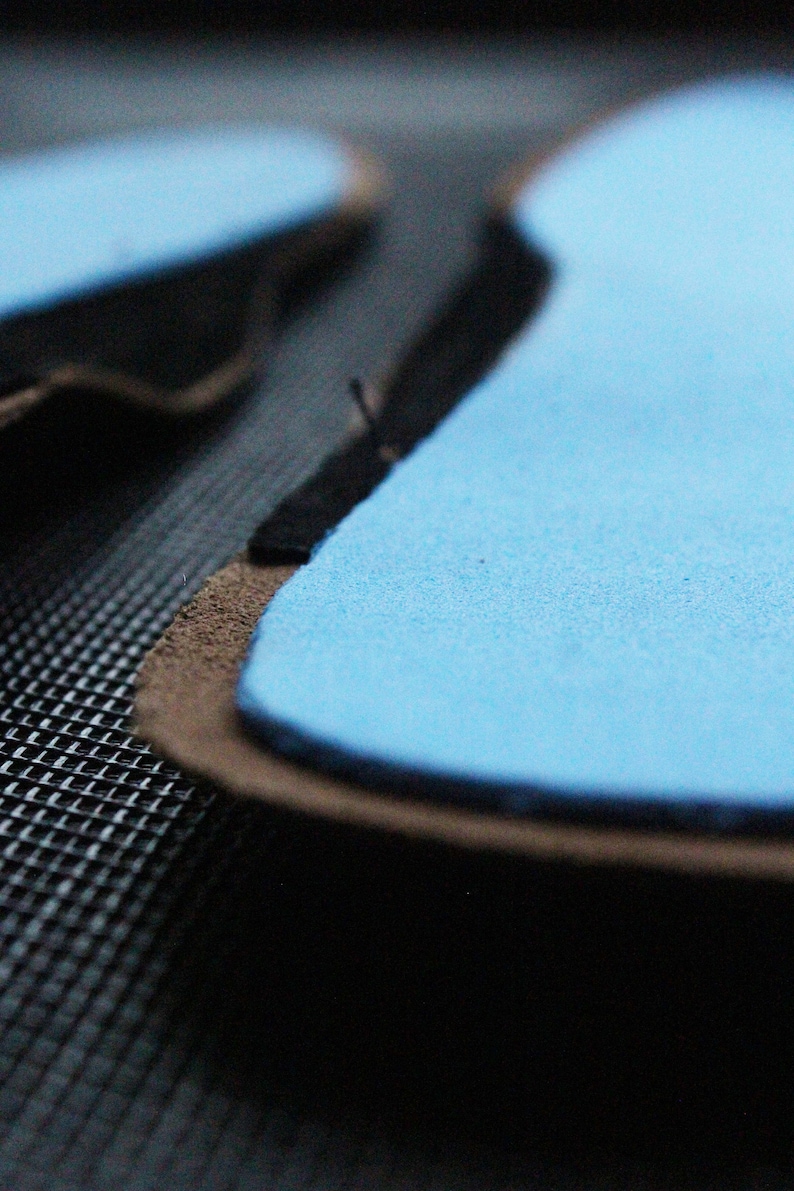 May include: Close-up of a light blue suede patch with a black stitched edge. The patch is on a dark gray textured surface.