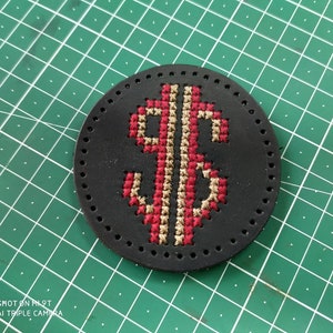 May include: A black leather coaster with a red and gold embroidered dollar sign.