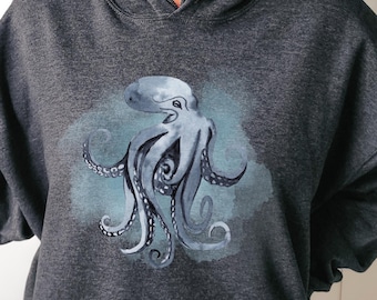 May include: Dark heather grey hoodie featuring a watercolour illustration of an octopus in shades of blue and grey.
