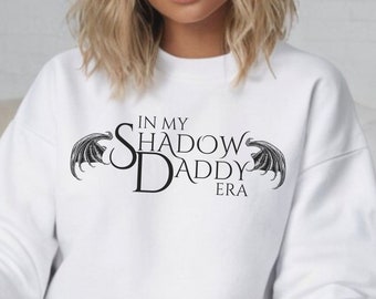 May include: White sweatshirt with black text and graphic that reads "In My Shadow Daddy Era" with two black wings on either side of the text.