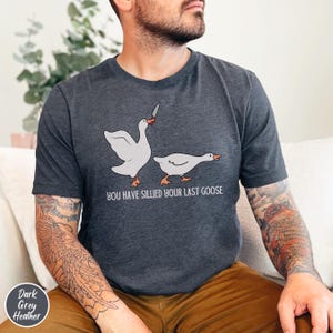 May include: Dark grey heather t-shirt with a white goose holding a knife and another goose running away. The text "You have sillied your last goose" is printed on the shirt.