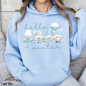 May include: Light blue hooded sweatshirt with a graphic of four gnomes holding gifts and a balloon. The text "hello winter" is printed on the sweatshirt.