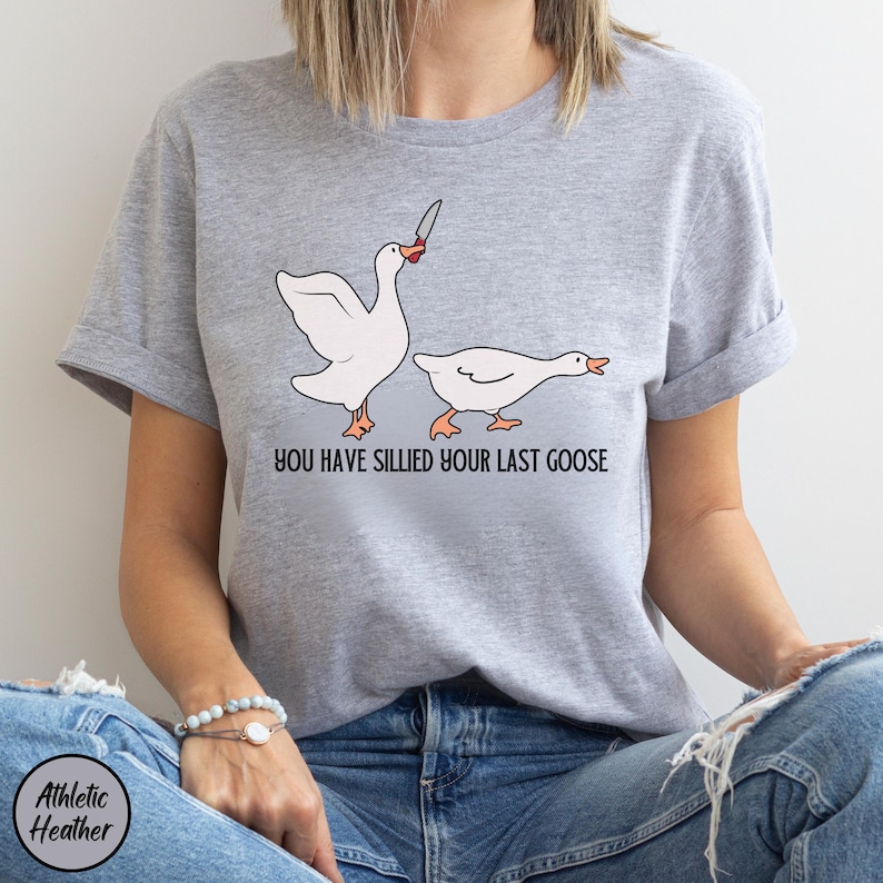 May include: A grey t-shirt with a graphic of two geese. The goose on the left is holding a knife and the text "You have sillied your last goose" is printed below the geese.