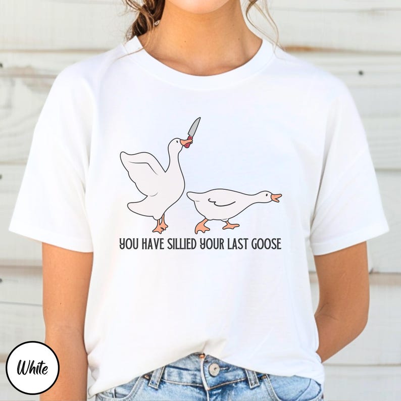 May include: White t-shirt with a graphic of two geese. One goose is holding a knife and the other goose is looking away. The text "You have sillied your last goose" is printed below the geese.