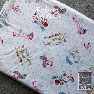 May include: White cotton fabric with a repeating pattern of whimsical illustrations and phrases. The design includes frogs, owls, apples, and text like "Live Our Dreams" and "Be Beautiful". The fabric is labeled "Fabric 100% Cotton".